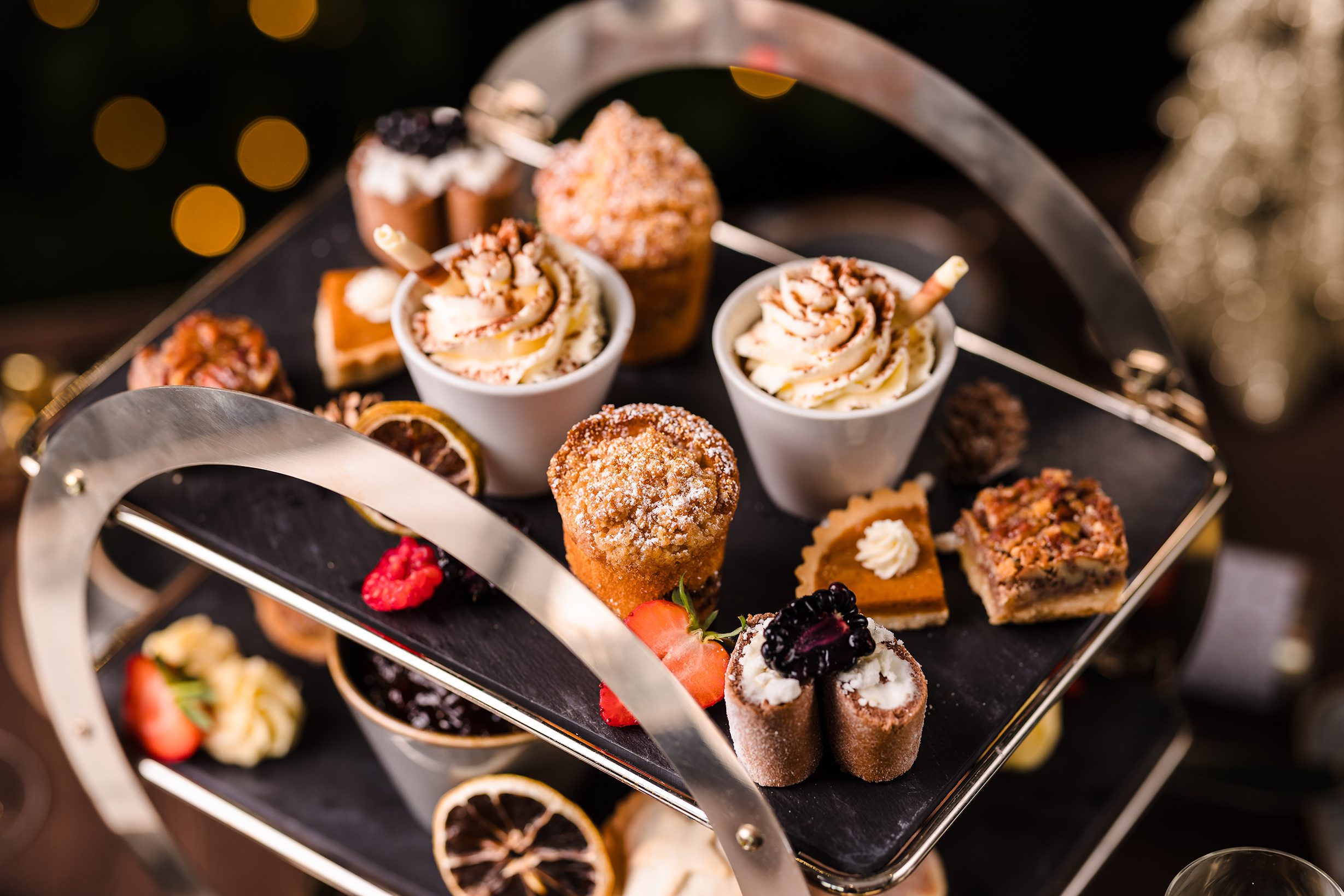 Assorted desserts for Christmas Eve Afternoon Tea, with cupcakes, tarts, and pastries on a two-tier black tray.
