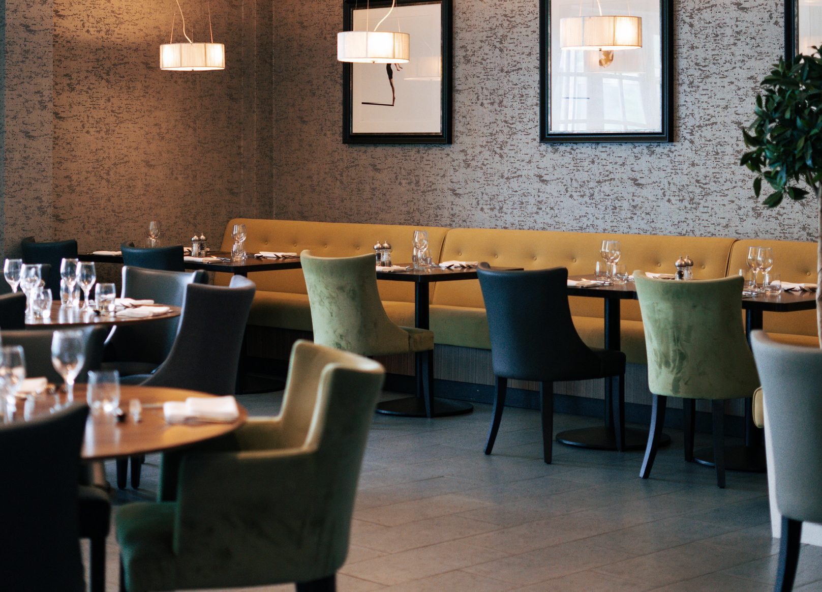 Modern restaurant interior with green and yellow chairs, set tables, wall art, pendant lighting, and vacancies available.