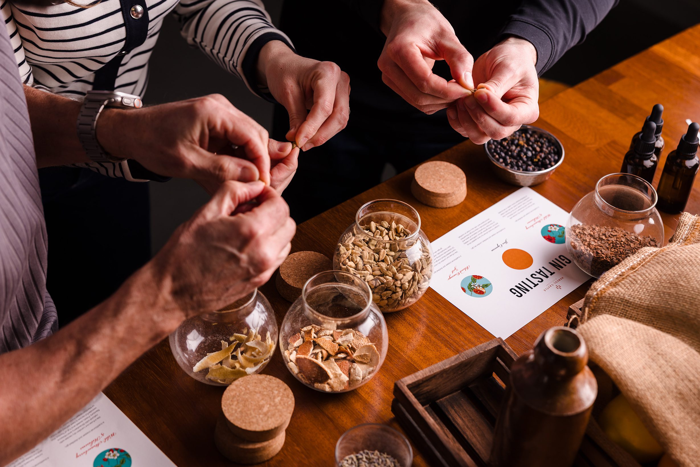 Three people prepare ingredients from glass jars on a table, planning meals and discussing hotel room bookings.