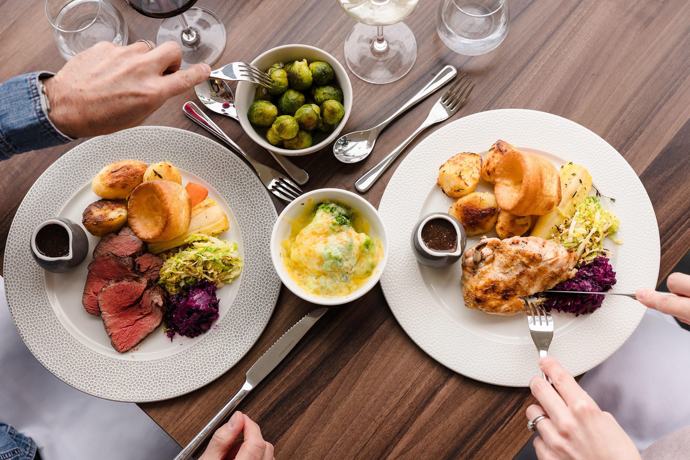 Two plates of roast dinners with vegetables and Yorkshire pudding, perfect for a cozy Sunday lunch on a wooden table.