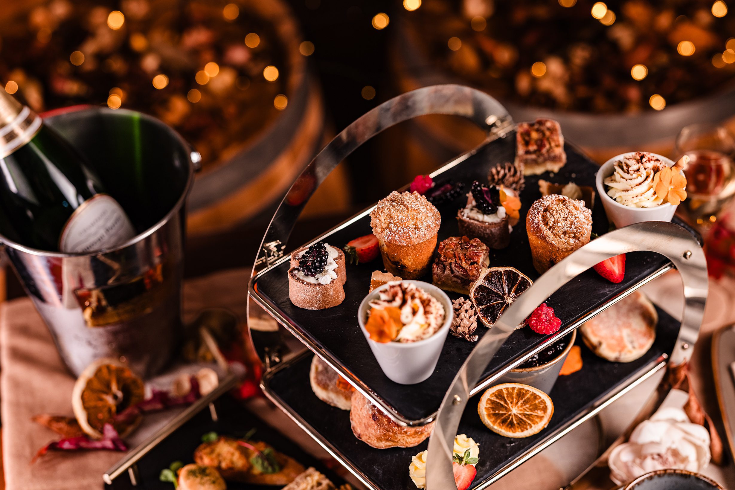 A two-tiered tray of assorted desserts, perfect for afternoon tea, with a champagne bottle chilling in an ice bucket.