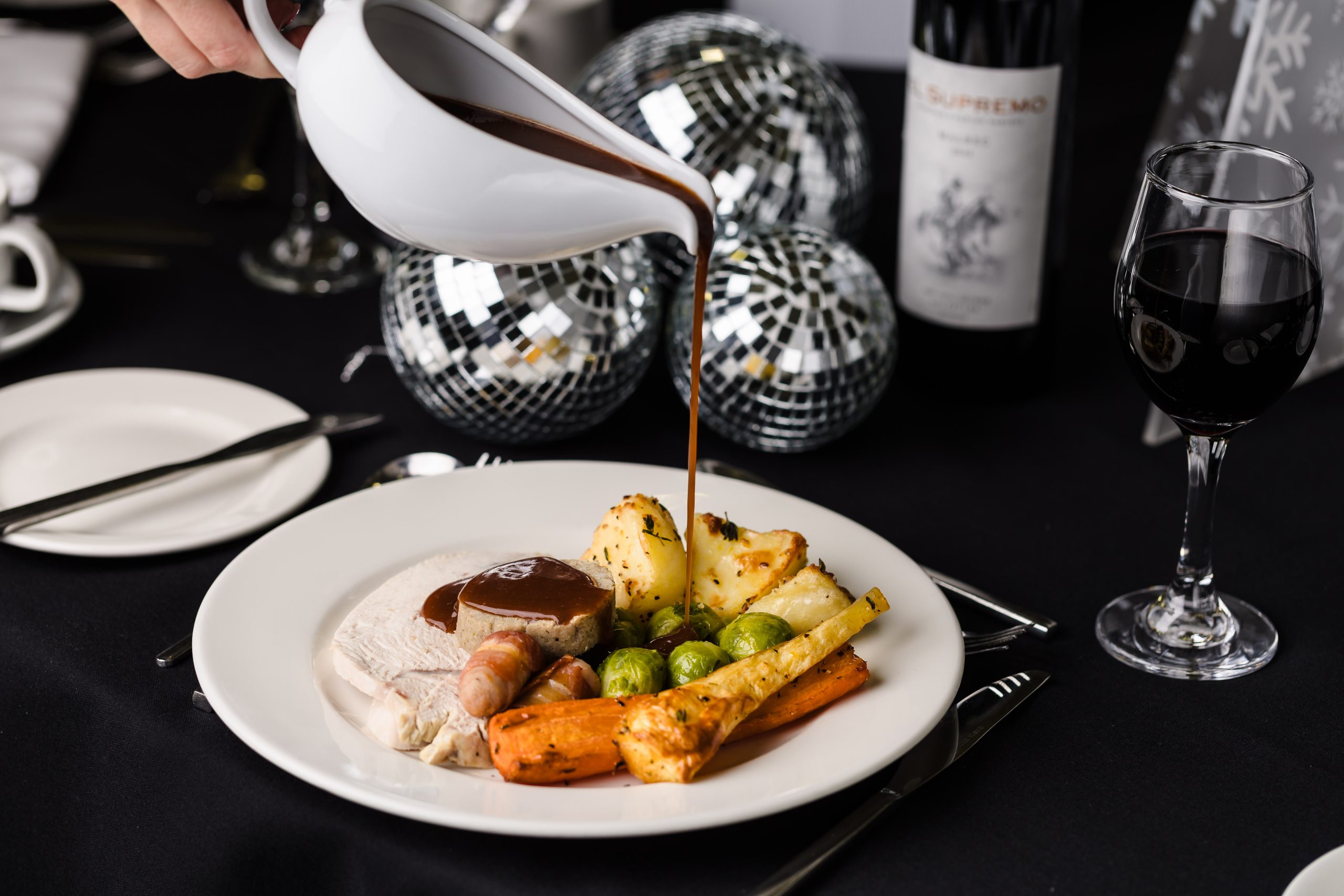 Perfect for a festive Christmas party, gravy is poured over turkey, veg, and pigs in blankets on a hearty plate.