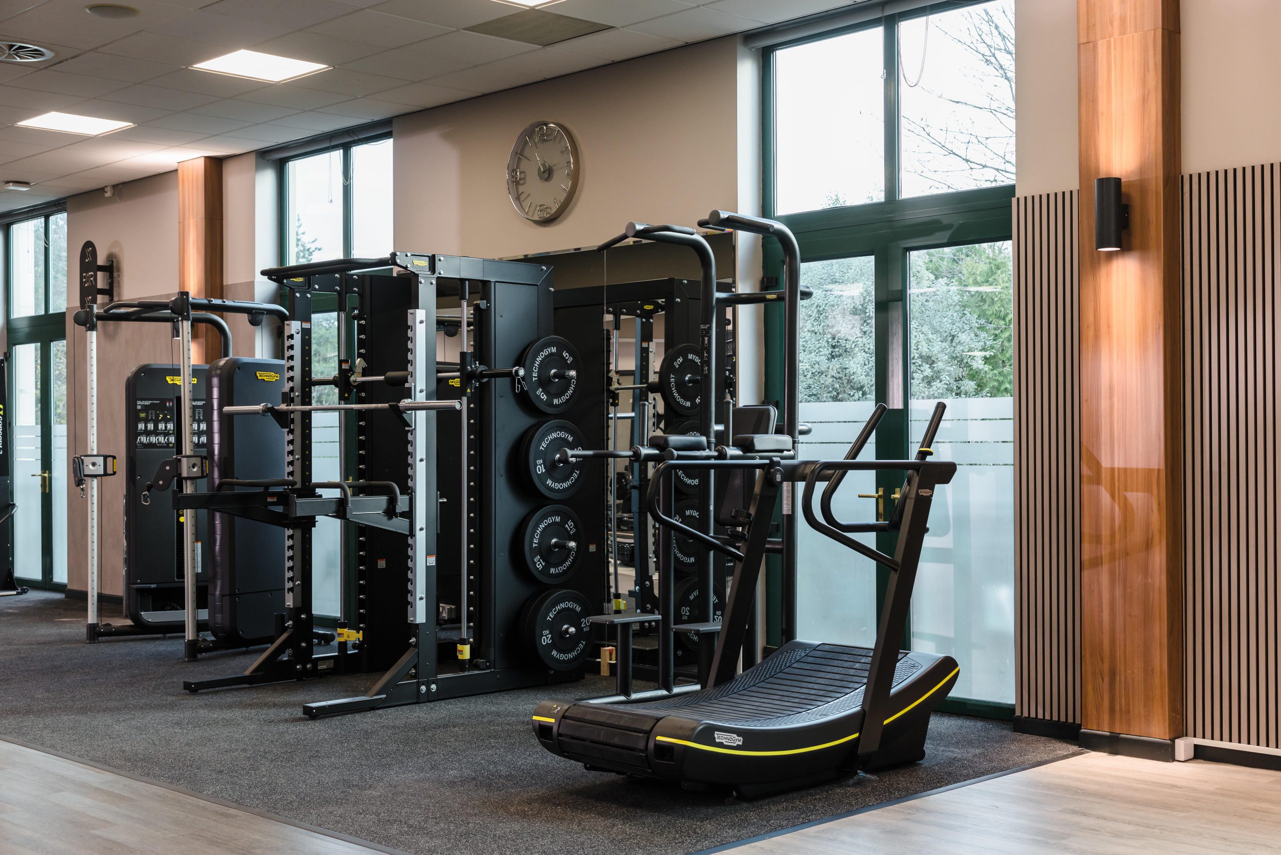 Modern Vale Resort South Wales Gym refurbished with weightlifting equipment, treadmill, large windows, and a wall clock.