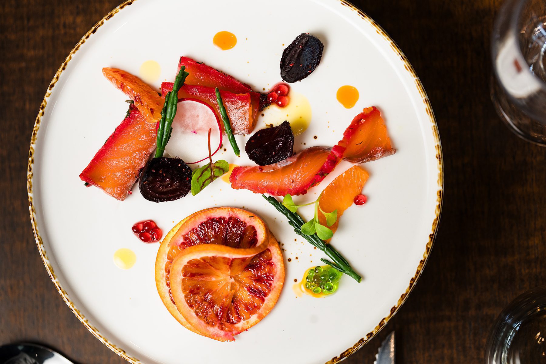 A white plate with cured fish, blood orange, beets, and microgreens—perfect for hotel breaks South Wales style.