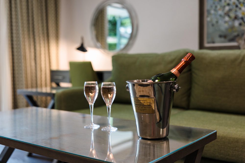 A bottle of champagne and flutes sit on a glass coffee table in the living room of luxury hotel rooms and suites.