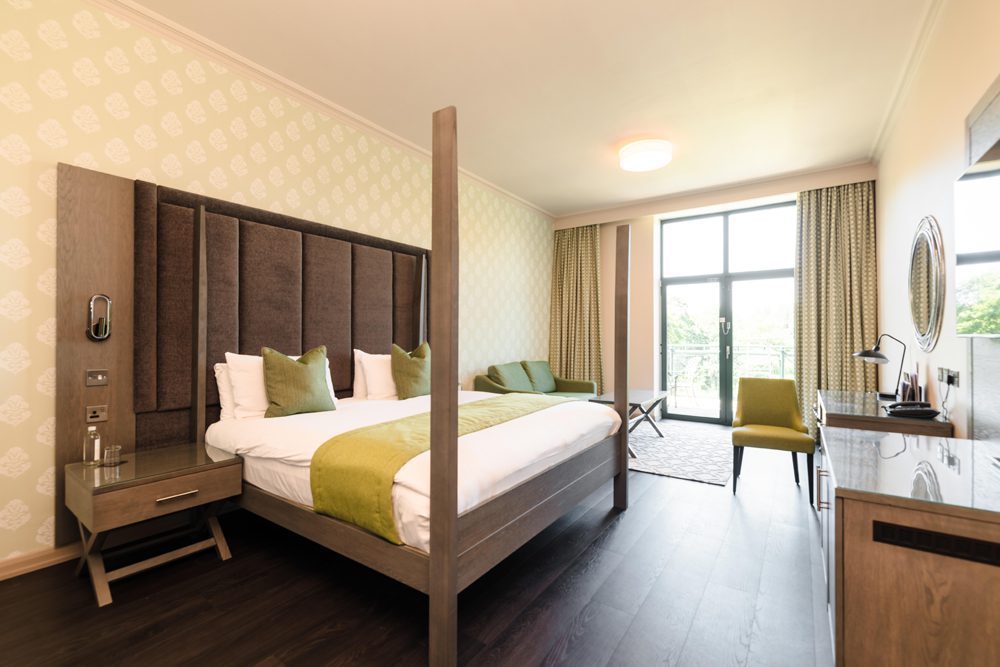 Modern hotel room with a large bed, green accents, and workspace—ideal for business events and dinners.