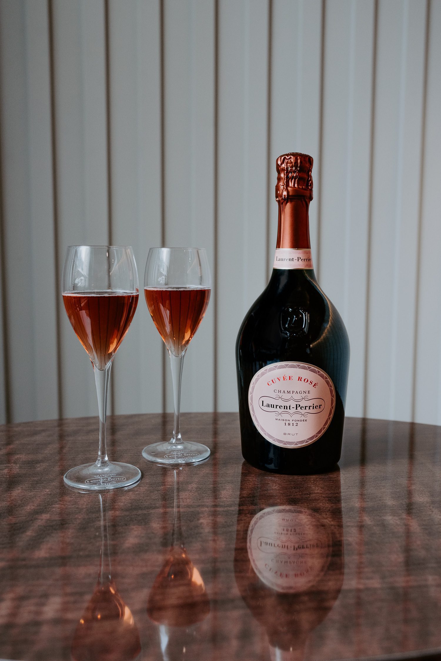 A bottle of Laurent-Perrier Cuvée Rosé Champagne is placed next to two filled champagne flutes on a table.