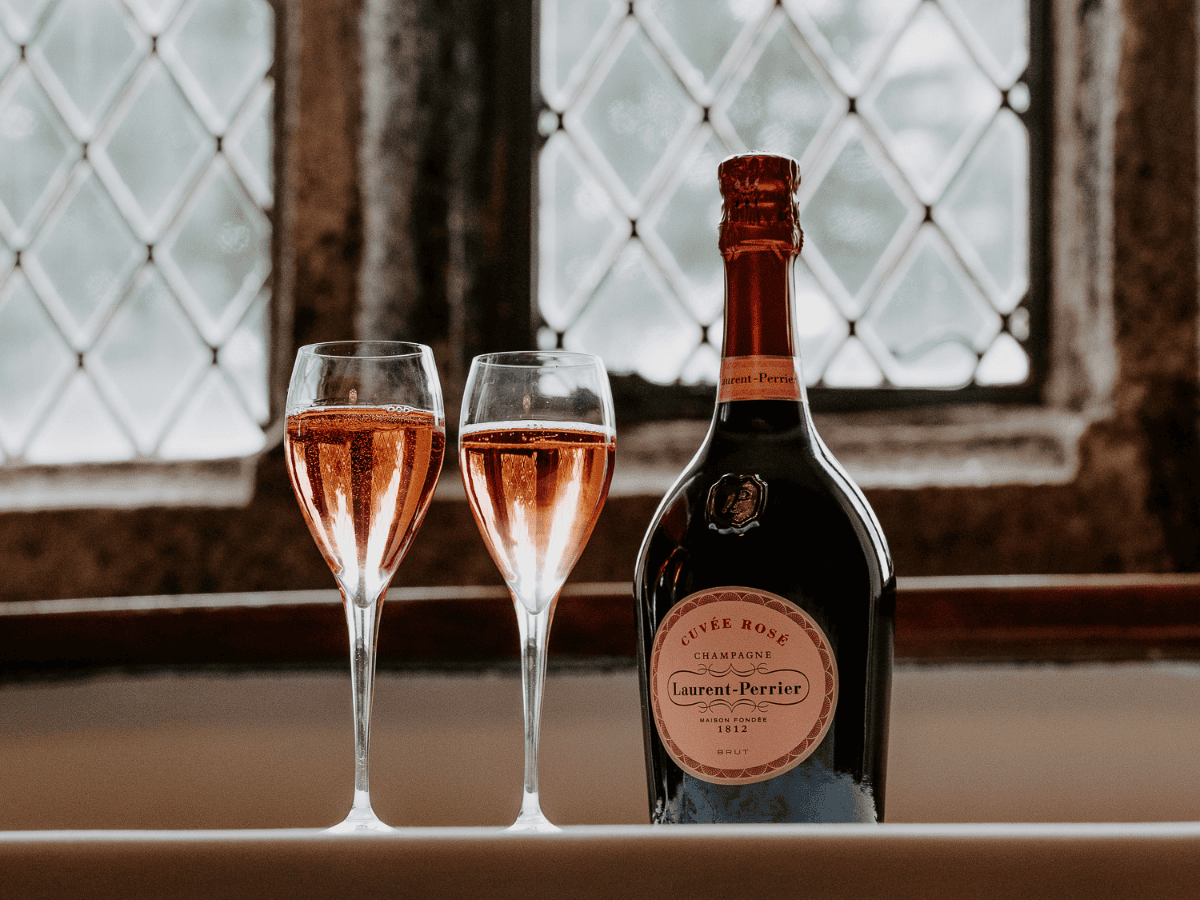 A bottle of Laurent-Perrier Cuvée Rosé champagne with two filled champagne flutes on a windowsill.
