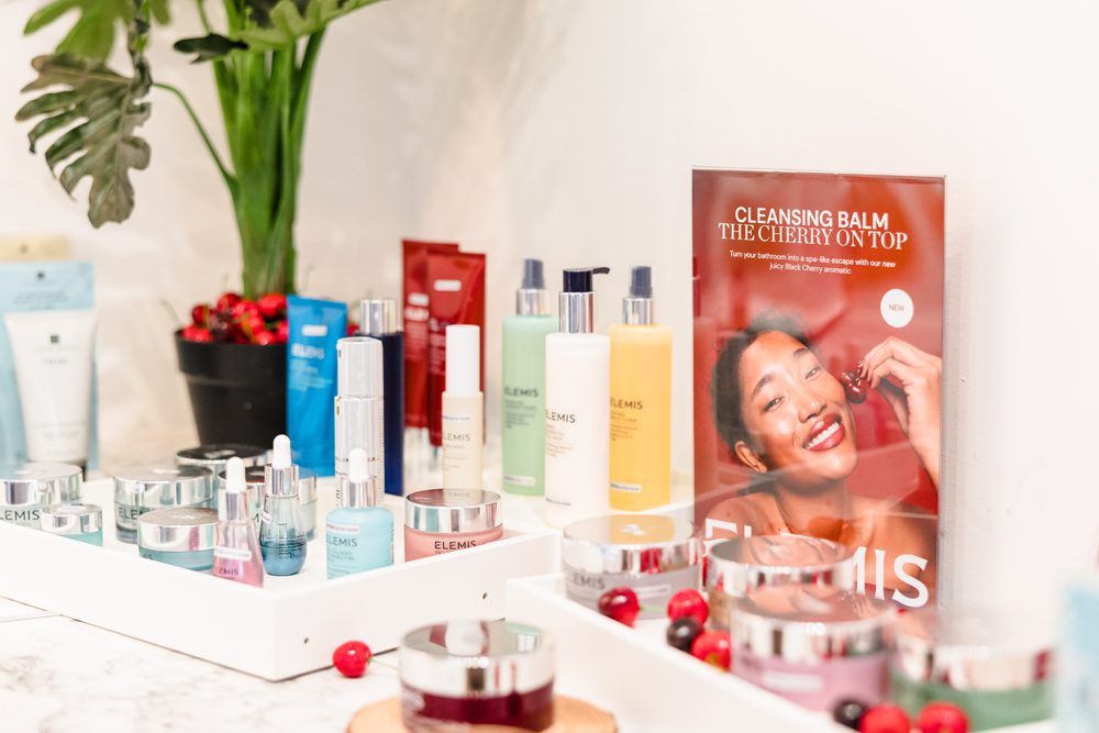 A display of skincare products, a plant, cranberries, and a spa facilities sign with a smiling woman on the bathroom counter.