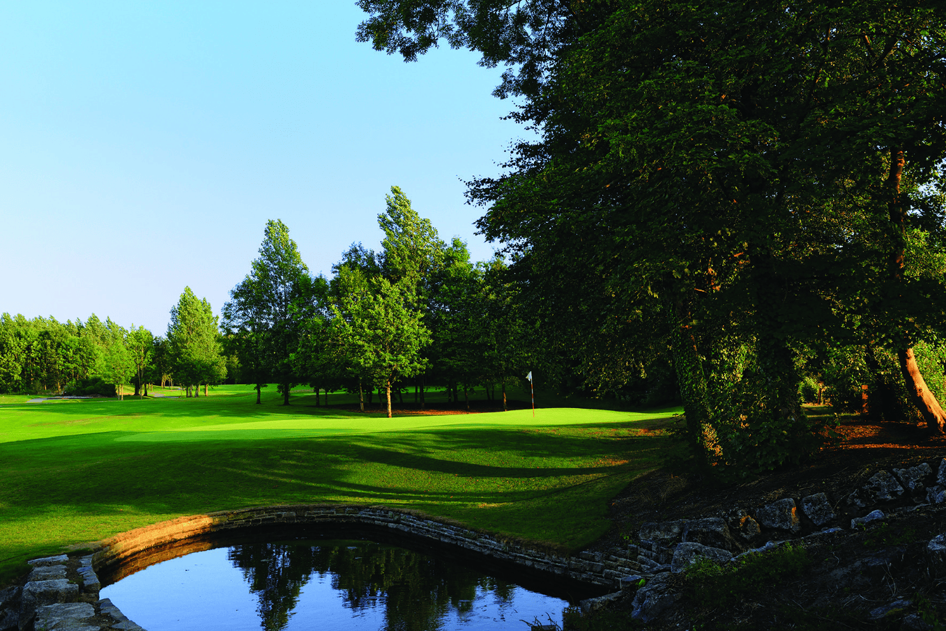 The National features green grass, scattered trees, and a small pond under a clear blue sky.