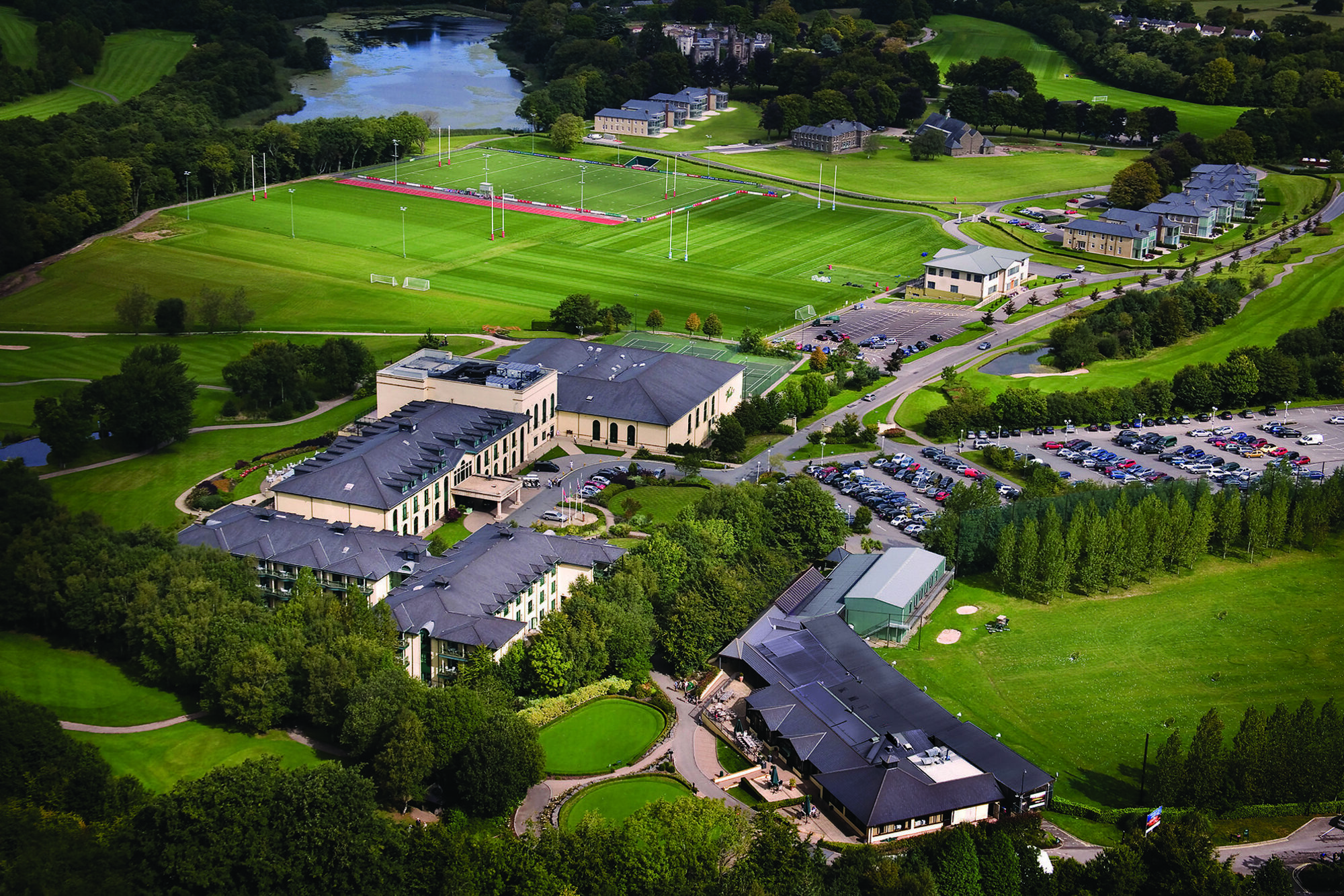 Aerial view of a historic destination featuring a large sports complex, multiple pitches, car parks, and lush greenery.